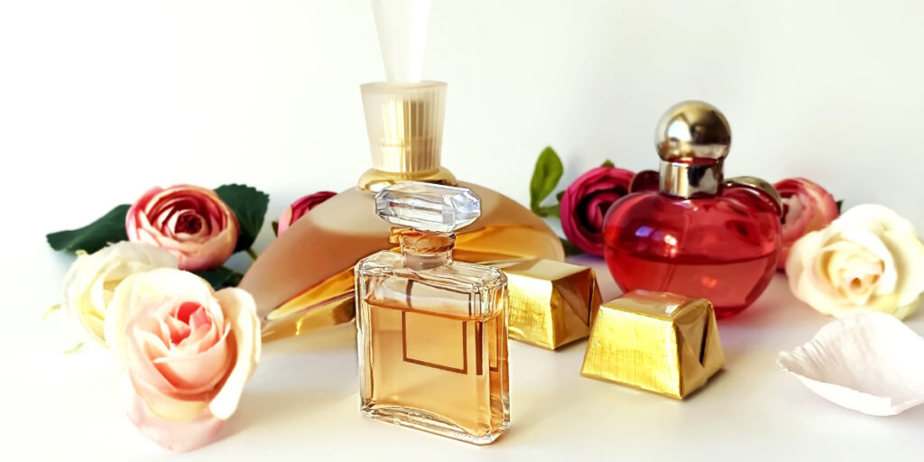 Elegant perfume bottles are surrounded by colorful roses and golden gift boxes on a white surface, creating a luxurious and aromatic setting.